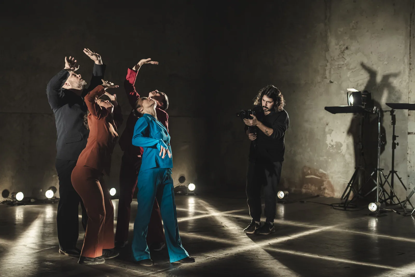 Five performers with raised arms in a warehouse, filmed by an operator with a gimbal